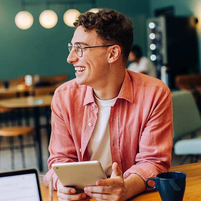 Guy holding a tablet sitting at a table.