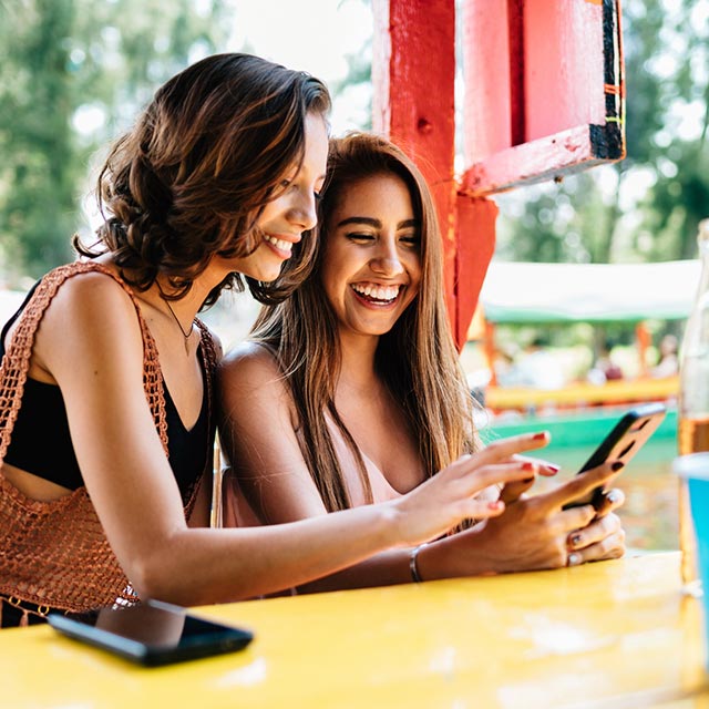 Friends looking at a phone at a colorful table.