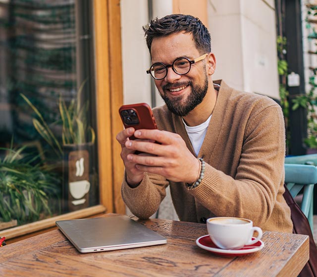 Man using his phone at a cafe with a laptop and cup of coffee.