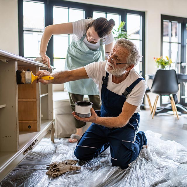 Man and woman applying stain to kitchen cabinets. 