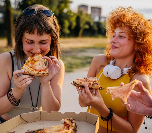 Two friends eating pizza outdoors.