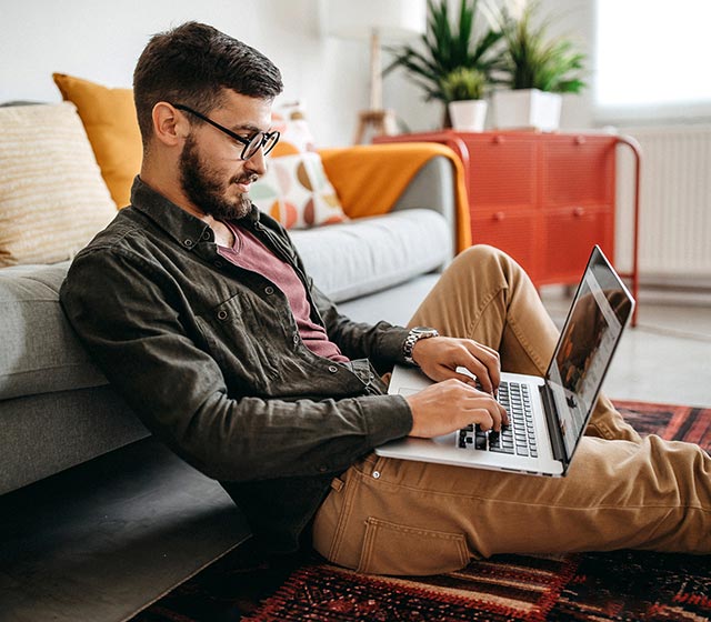 Man sitting on the floor typing on his laptop.
